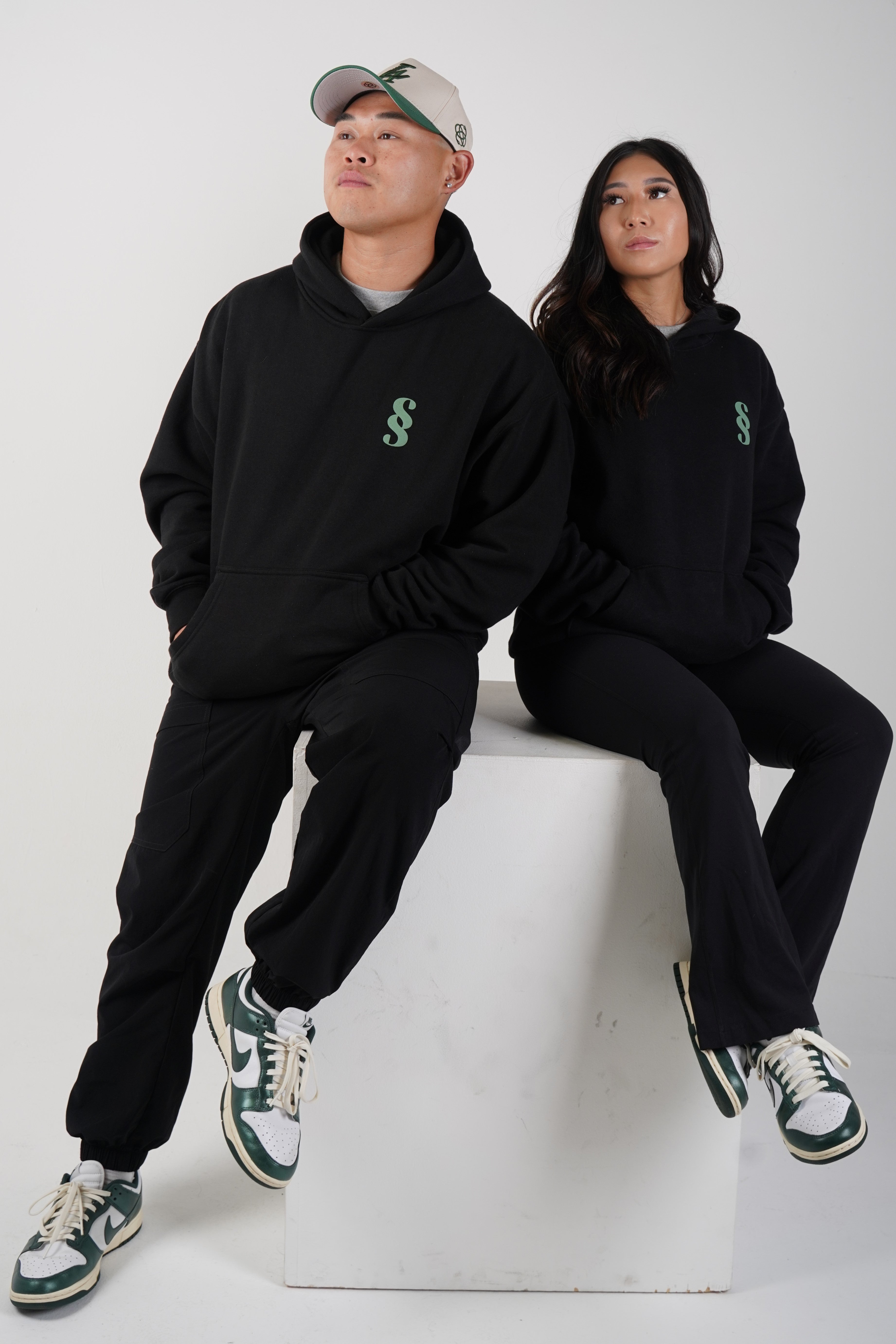 stacey and steven sitting looking away wearing the ssalary hoodie